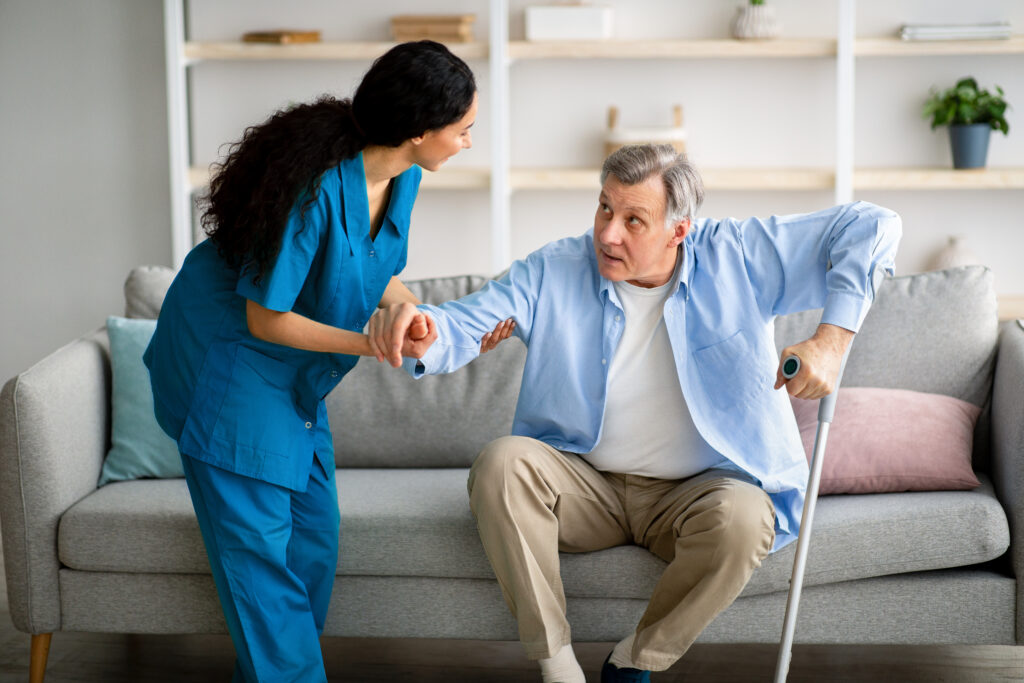 caregiver helping senior man with crutch